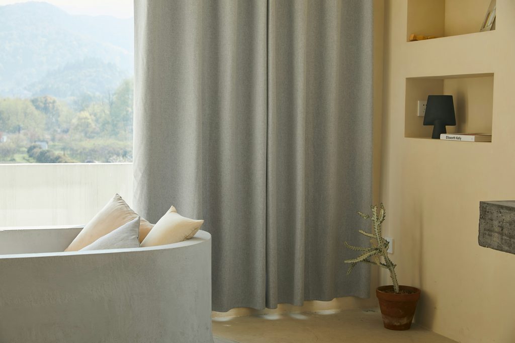 Minimalist room with bathtub, pillows, and gray curtains.