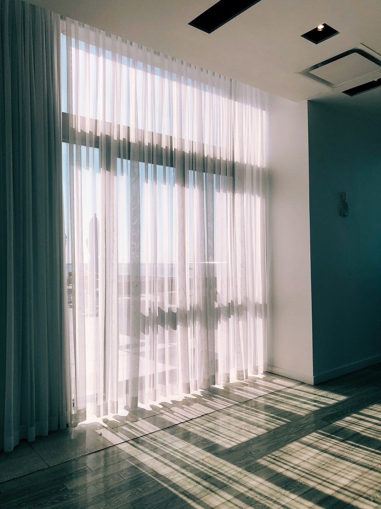 Sunlight through sheer white curtains onto wooden floor.