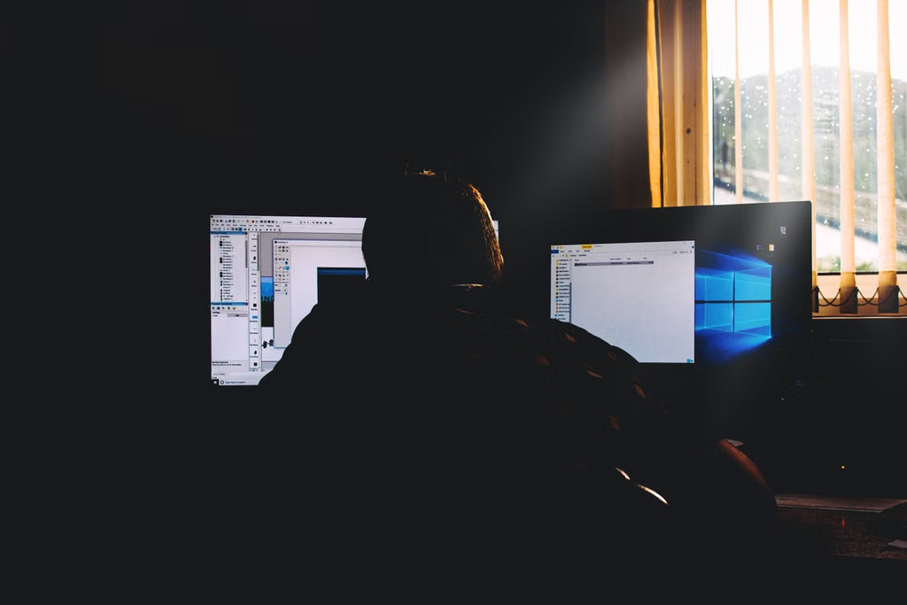 Person working on computer screens in dim room.